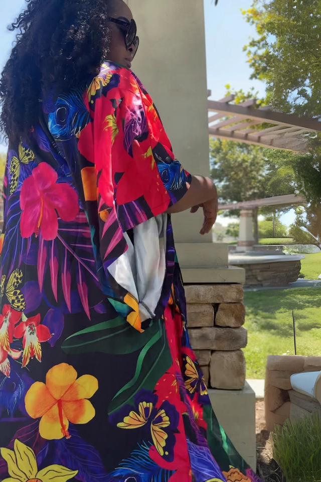 Person wearing a colorful floral dress standing outdoors with greenery in the background